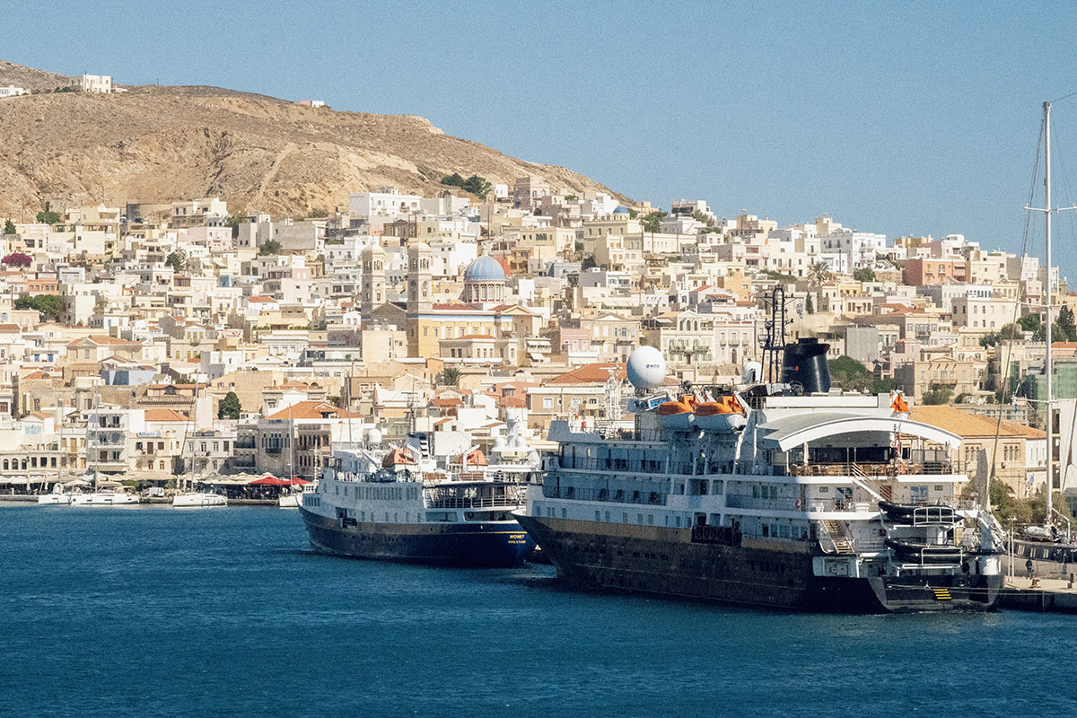 A ferry arriving at the port of Ermoupoli, Syros, with the neoclassical town and its two hills rising behind the harbor. Daylight arrival into the capital of the Cyclades.